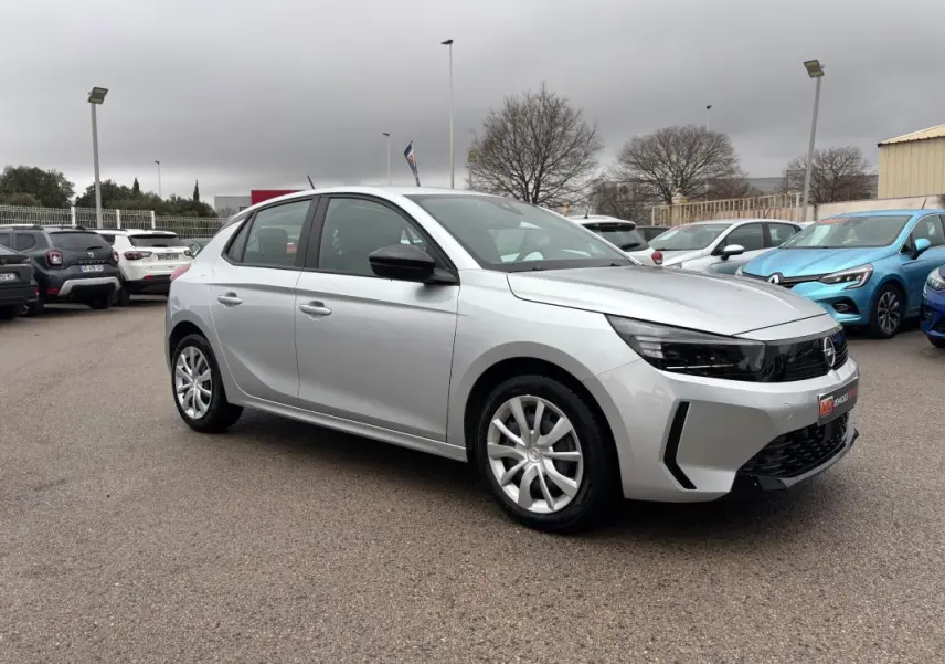 Opel Corsa gris clair vue 3/4 avant droit, avec jantes classiques et rétroviseurs noirs contrastants.