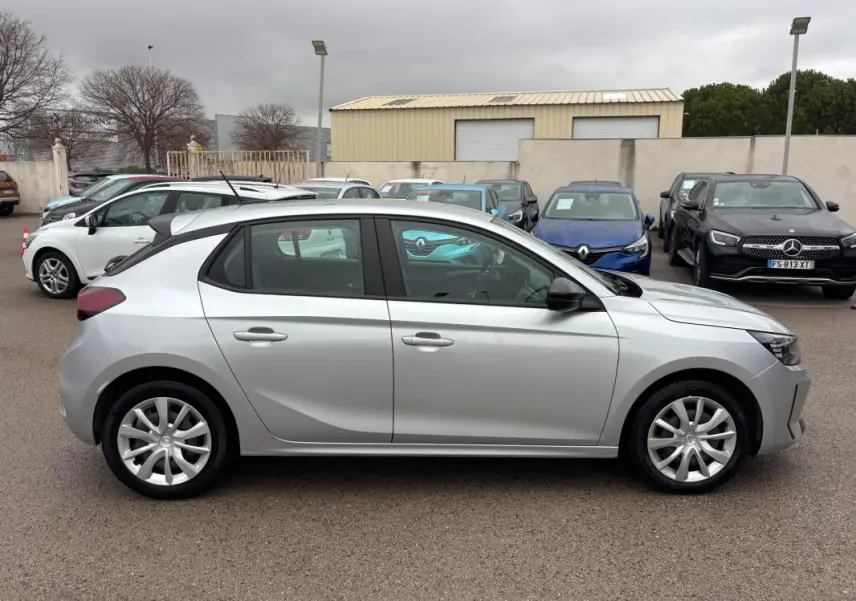 Vue latérale droite d'une Opel Corsa gris clair 2024 avec jantes classiques, garée en extérieur sur un parking.