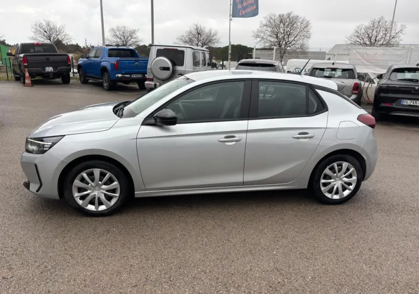 Opel Corsa gris clair vue de profil côté gauche, avec jantes classiques et rétroviseurs noirs.