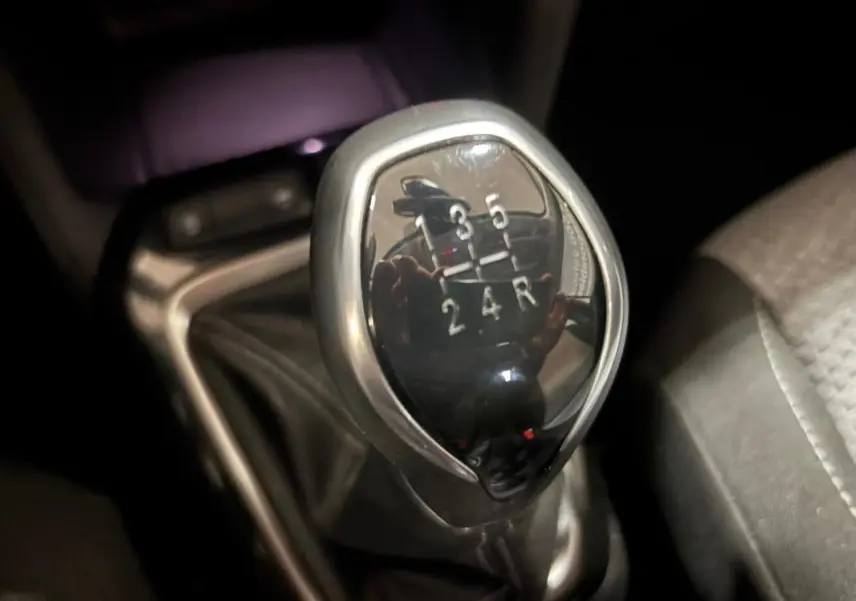 Gros plan sur le levier de vitesses manuel noir et chrome de l’Opel Corsa gris clair, intérieur sombre.