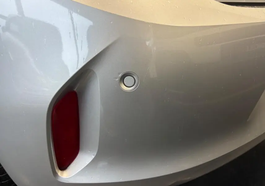 Gros plan sur le pare-chocs arrière gris clair de l'Opel Corsa 2024 avec capteur de recul et feu rouge intégré.