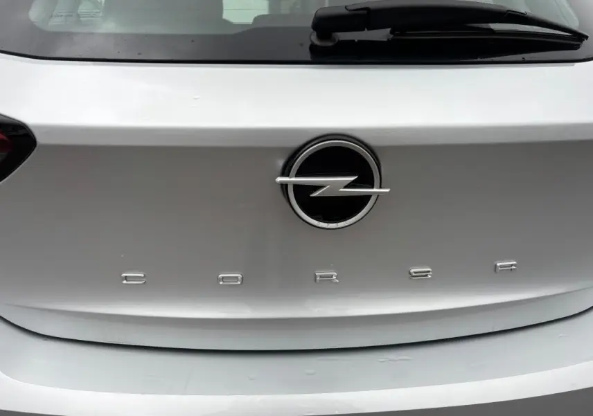 Gros plan sur le logo Opel et l'inscription Corsa à l'arrière d'une voiture gris clair.