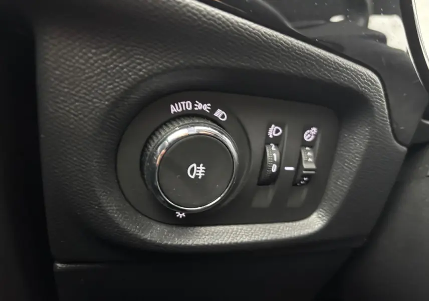 Gros plan sur le bouton de commande des feux avec réglages automatiques dans l’habitacle noir de l’Opel Corsa gris clair.