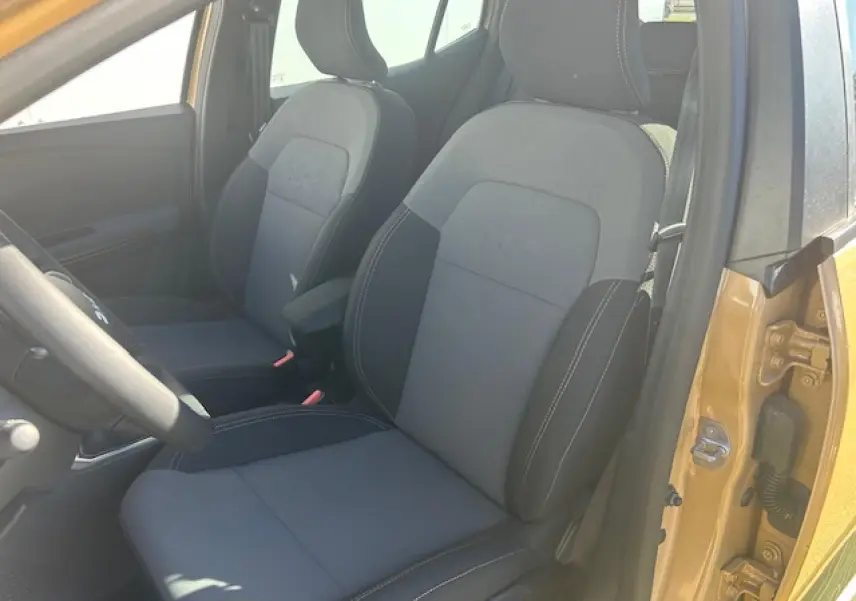 Vue intérieure côté conducteur de la Dacia Sandero III Stepway beige Safari, avec sièges noirs et accoudoir central.