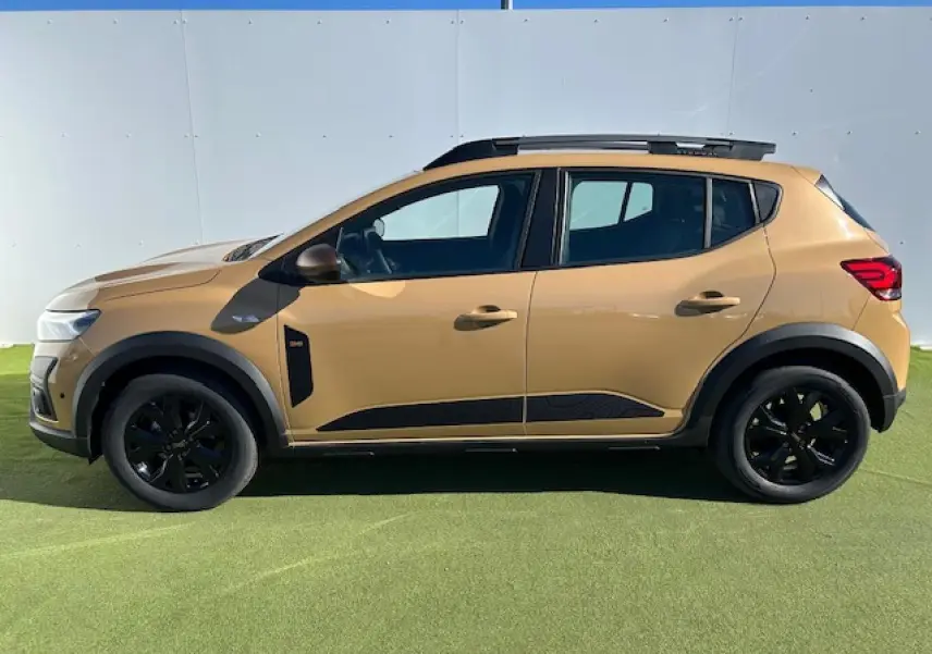 Profil droit de la Dacia Sandero Stepway beige Safari 2025 avec barres de toit et jantes noires.