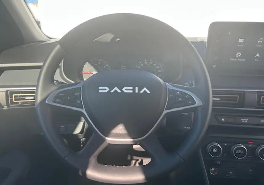 Vue centrée sur le volant noir du Dacia Sandero III Stepway avec tableau de bord et écran tactile visible.