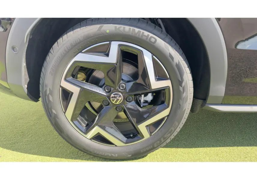 Gros plan sur la roue avant droite du Volkswagen T-Roc noir avec jante 18 pouces bicolore et logo VW au centre.