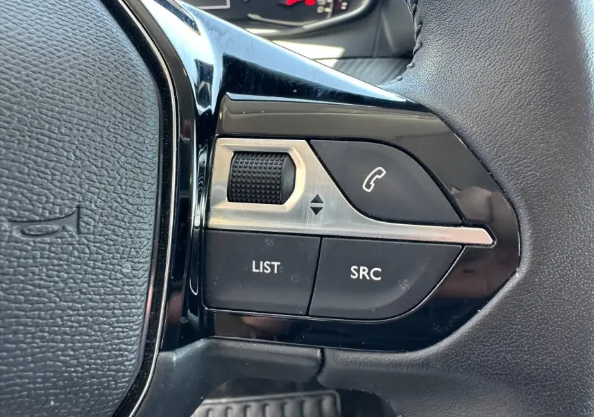 Gros plan sur les commandes audio au volant noir de la Peugeot 208 1.2 100ch Style, avec molette et boutons fonctionnels.