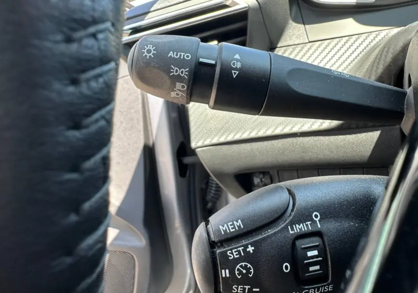 Gros plan sur les commandes de régulateur et feux au volant d’une Peugeot 208 gris Artense, intérieur noir.