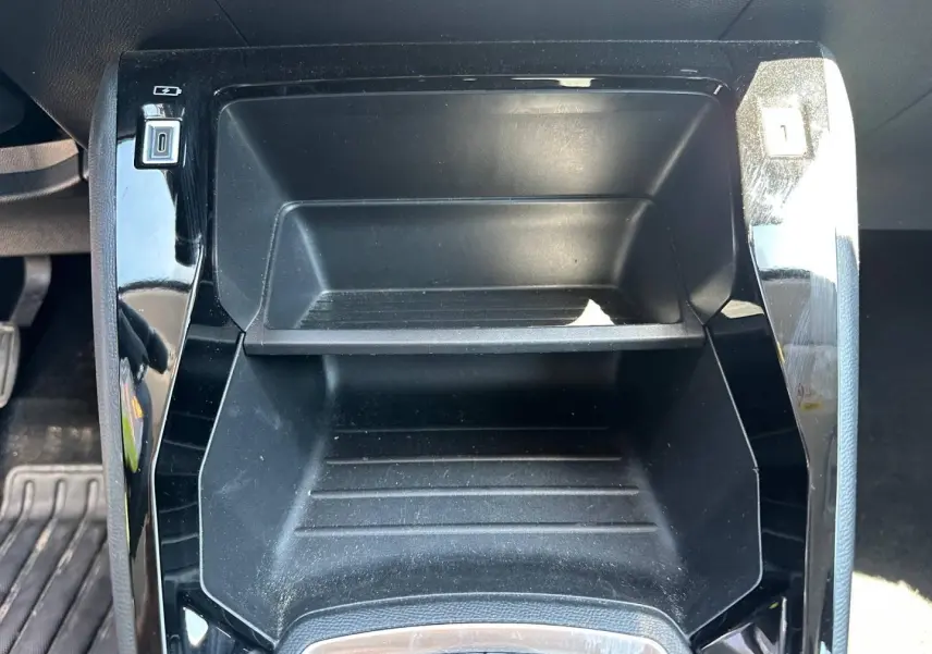 Gros plan sur le rangement central noir brillant de la Peugeot 208 1.2 100ch Style, avec ports USB visibles.