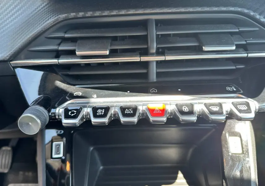 Vue rapprochée de la console centrale de la Peugeot 208 2025, boutons de commande argentés et noir avec bouton rouge d’alerte.