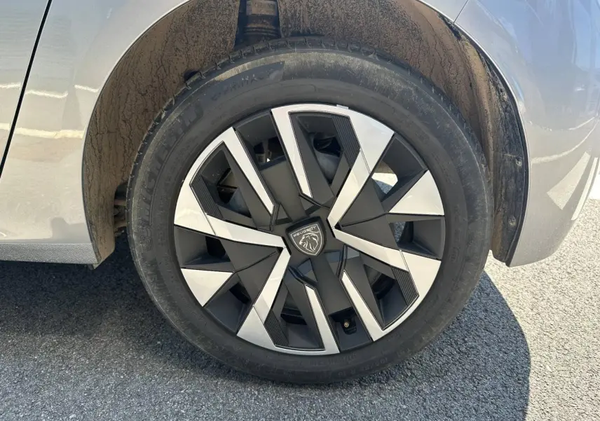 Gros plan sur la roue arrière droite d’une Peugeot 208 gris Artense avec jante au design géométrique noir et argent.