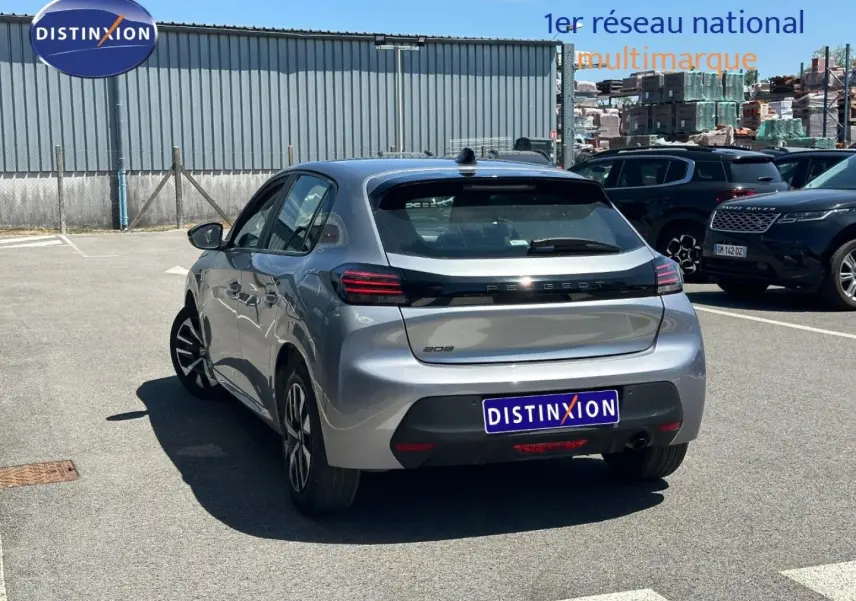 Vue 3/4 arrière droite d'une Peugeot 208 gris Artense garée sur un parking extérieur ensoleillé.