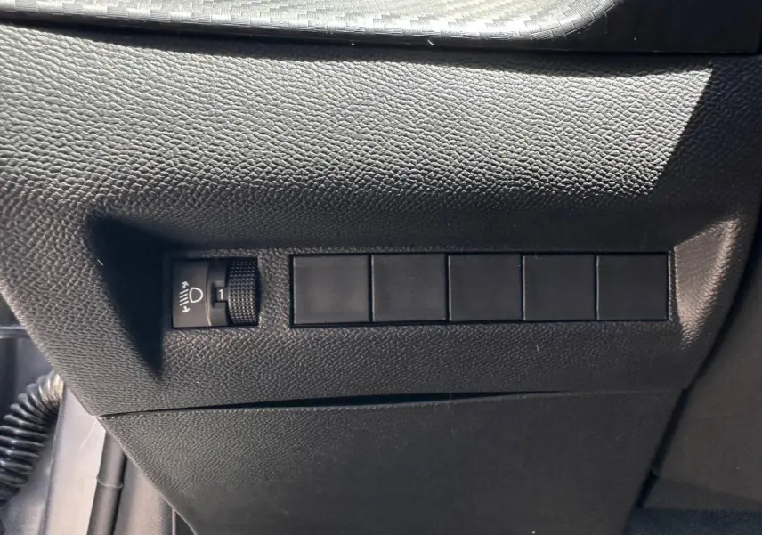 Détail du tableau de bord côté gauche avec réglage de hauteur des phares sur Peugeot 208 Gris Artense.