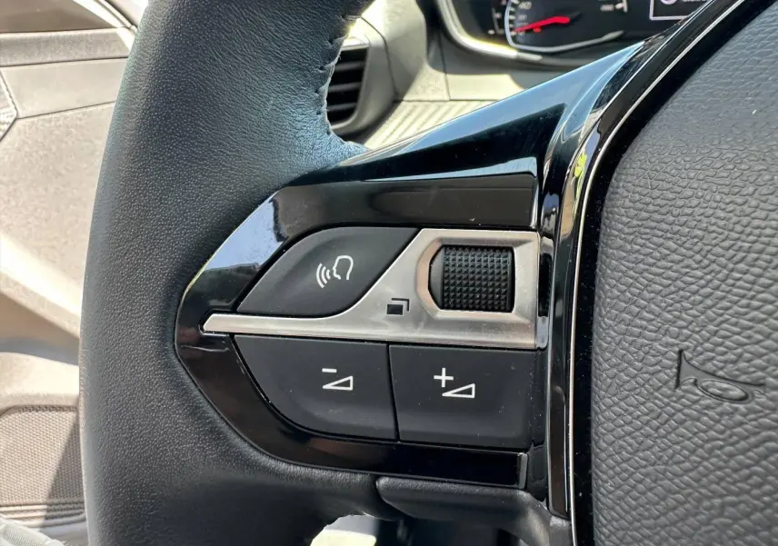 Gros plan sur les commandes audio au volant noir de la Peugeot 208 1.2 100ch Style, intérieur gris.