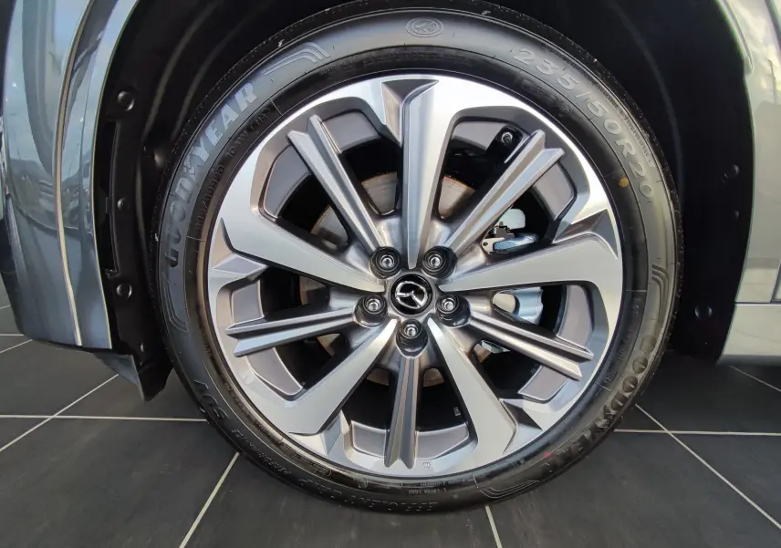 Gros plan sur la jante alliage 20 pouces du Mazda CX-80 gris foncé, mettant en valeur le logo Mazda central.