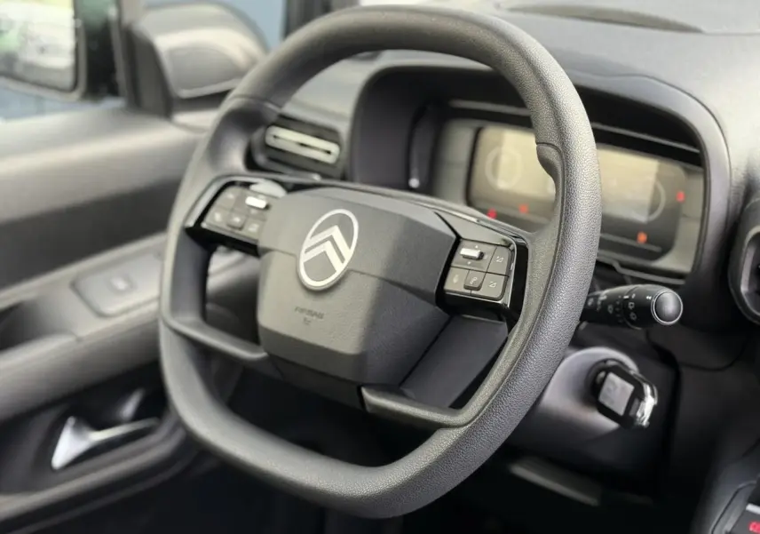 Volant multifonctions noir de Citroën Berlingo 2025, vue rapprochée côté conducteur avec tableau de bord numérique flou.