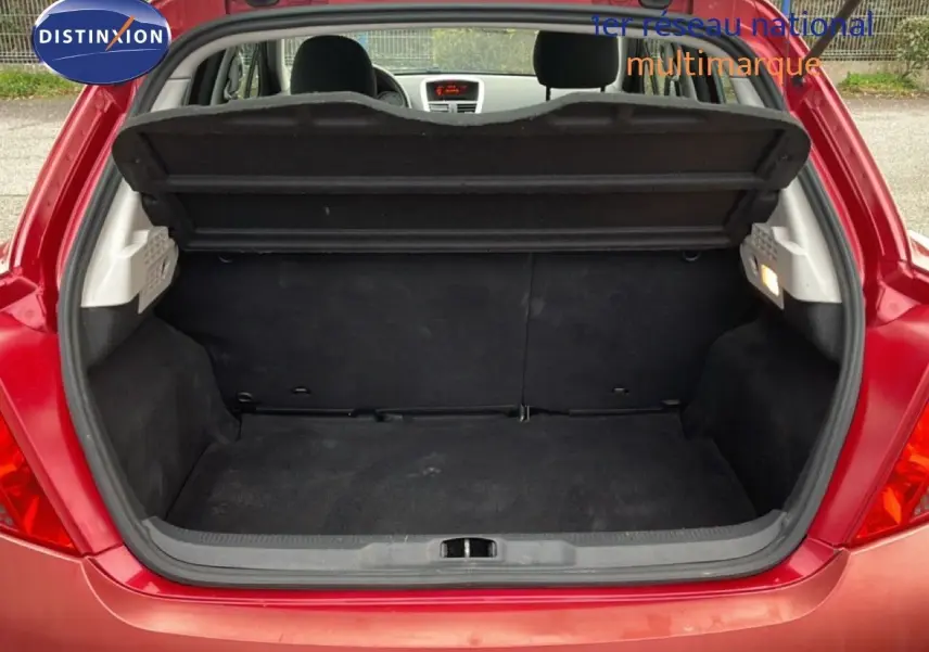 Coffre ouvert d'une Peugeot 207 rouge métal vue arrière, montrant l'espace de chargement et la banquette arrière.