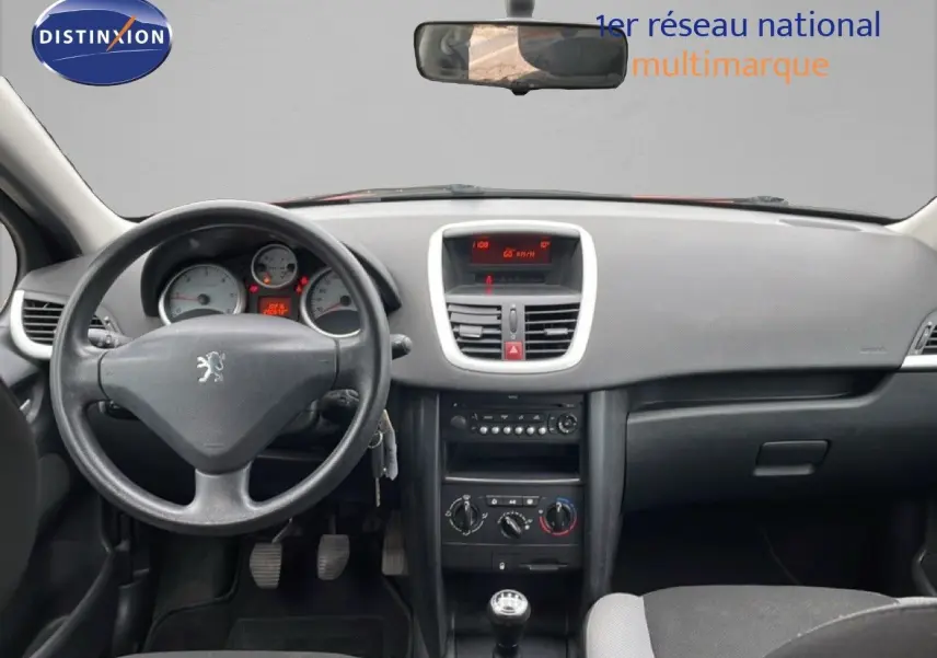 Vue intérieure avant du tableau de bord et volant noir d'une Peugeot 207 rouge métal de 2009 avec boîte manuelle.