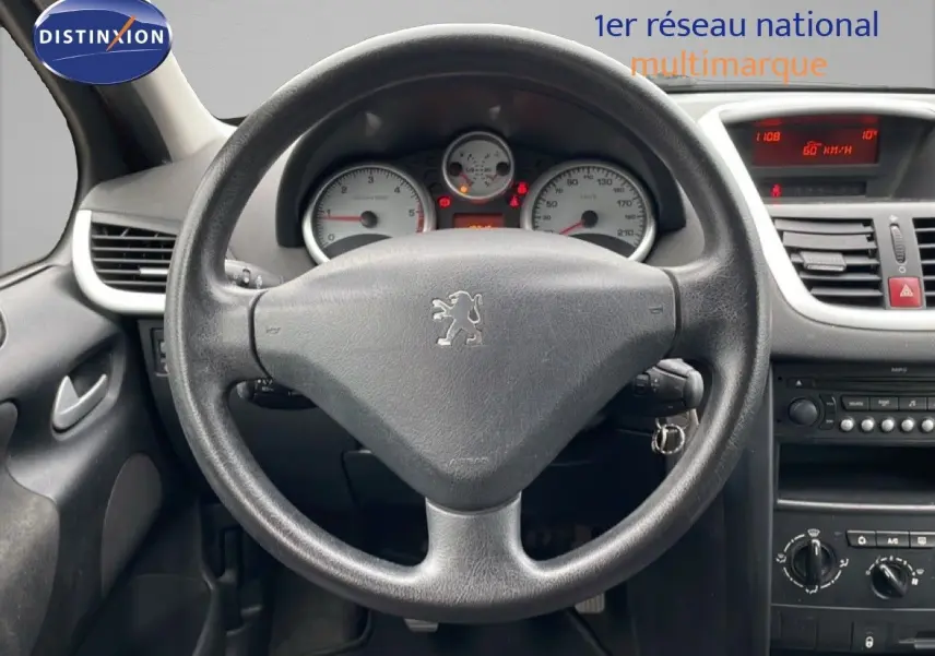 Vue intérieure centrée sur le volant noir de la Peugeot 207 HDI 70CH Trend de 2009 avec tableau de bord et commandes visibles.