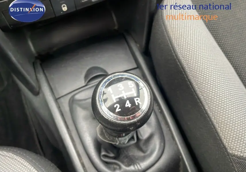 Le levier de vitesse manuel noir de la Peugeot 207 HDI 70CH TREND, entouré de sièges en tissu gris.