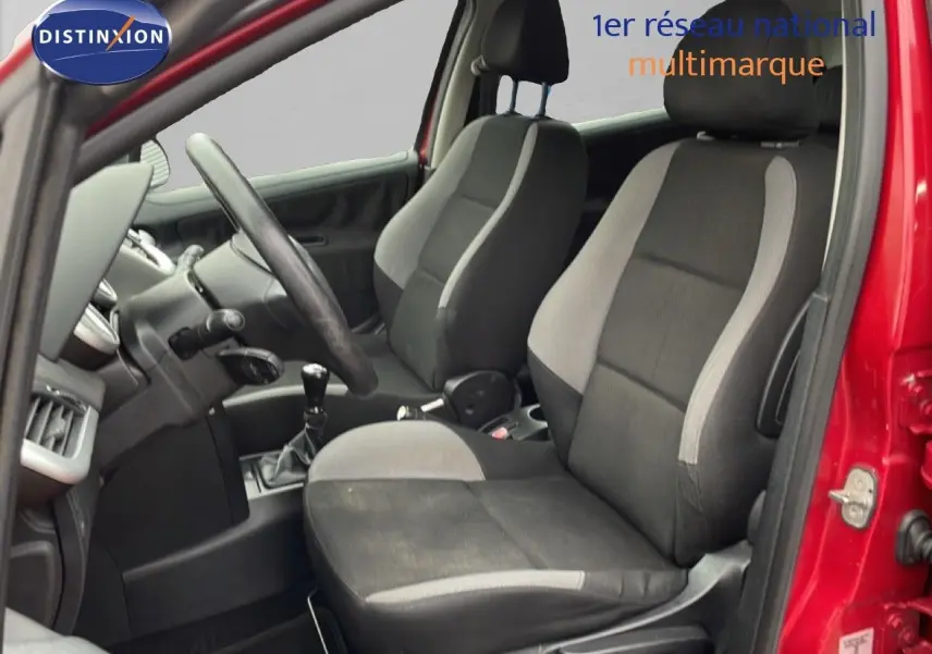 Intérieur de la Peugeot 207 rouge métal 2009, vue côté gauche, sièges tissu noir et gris avec levier de vitesse manuel.