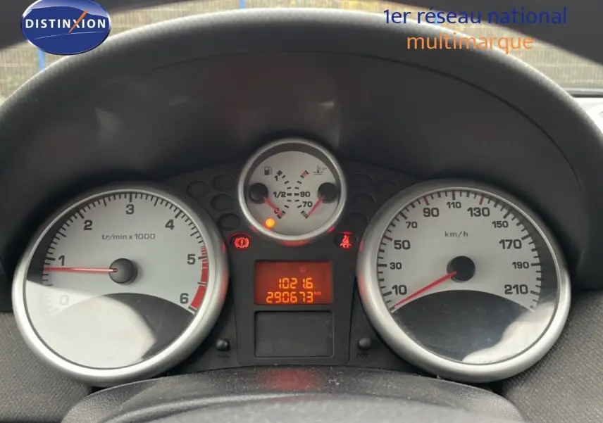 Vue rapprochée du tableau de bord de la Peugeot 207 rouge métal, montrant les compteurs et l'odomètre digital.
