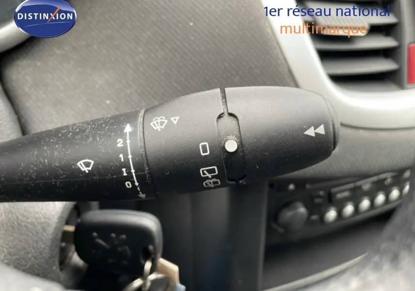 Gros plan sur la commande d’essuie-glace à gauche du volant dans l’habitacle d’une Peugeot 207 rouge métal de 2009.