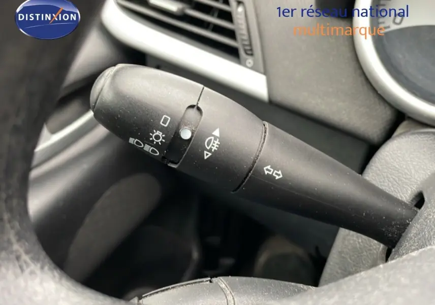Gros plan sur la commande de clignotants à gauche du volant d'une Peugeot 207 rouge métal de 2009.