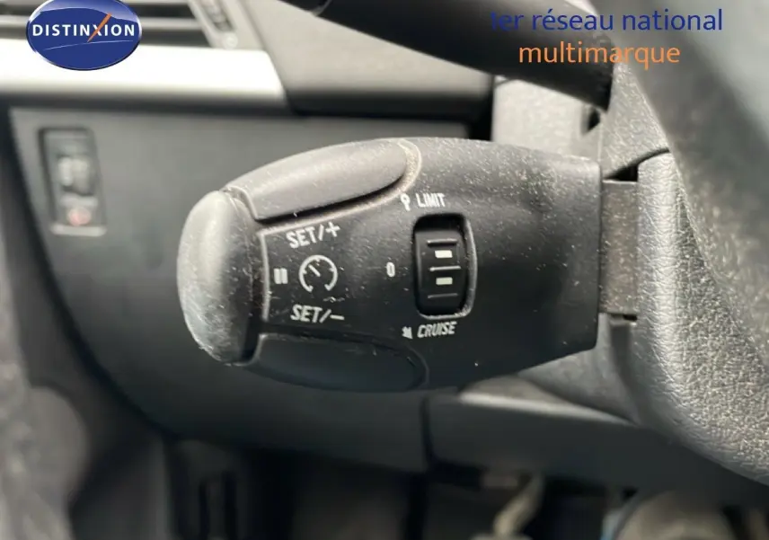 Gros plan sur la commande de régulateur de vitesse au volant d'une Peugeot 207 rouge métal de 2009.