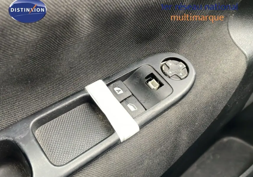 Gros plan sur les commandes de lève-vitres côté conducteur d'une Peugeot 207 rouge métal de 2009.