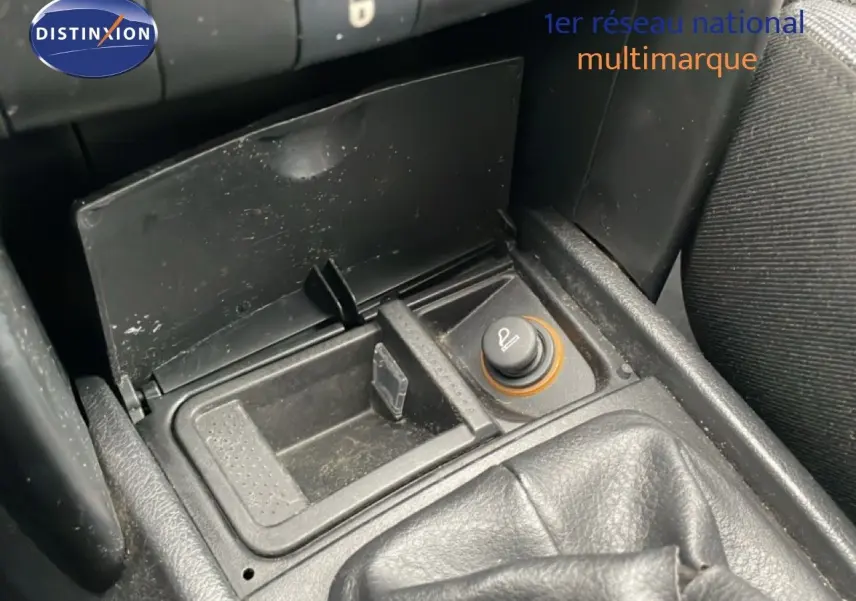Gros plan sur la console centrale de la Peugeot 207 rouge métal, montrant l'allume-cigare et le soufflet de levier de vitesses.
