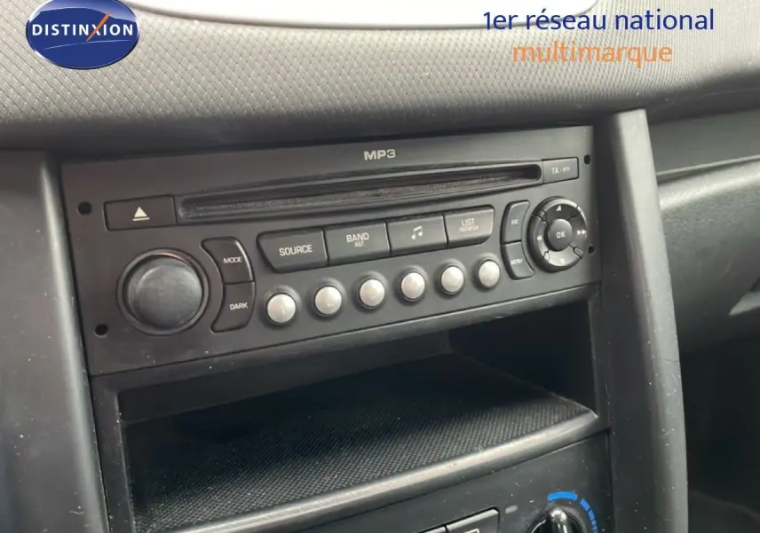 Vue rapprochée de la console centrale noire de la Peugeot 207 rouge métal, mettant en valeur la radio MP3 et les commandes climatiques.