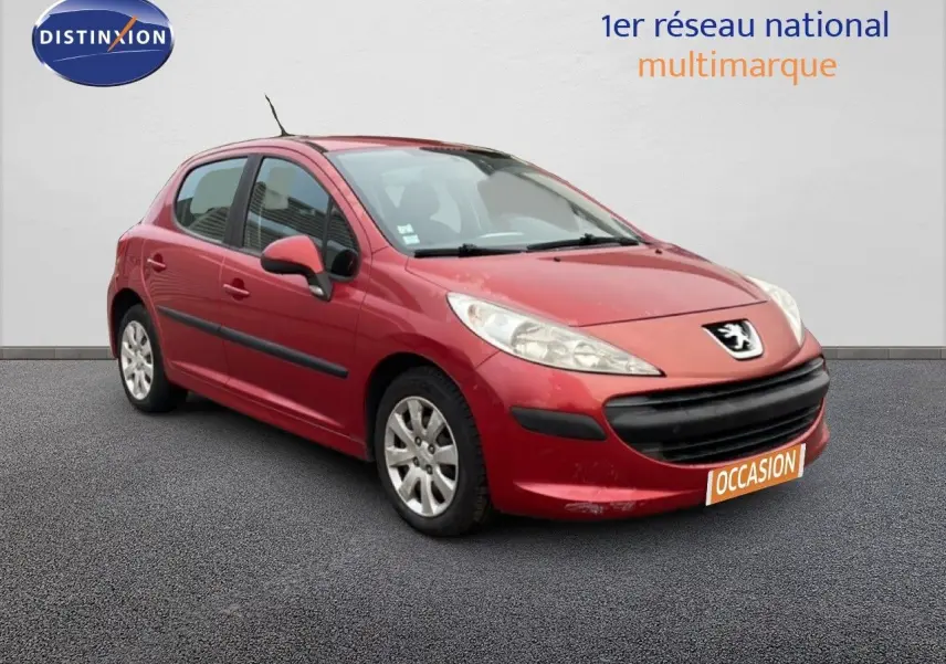 Peugeot 207 rouge métal vue 3/4 avant droit, compacte 5 portes avec pare-chocs noir et jantes alliage.