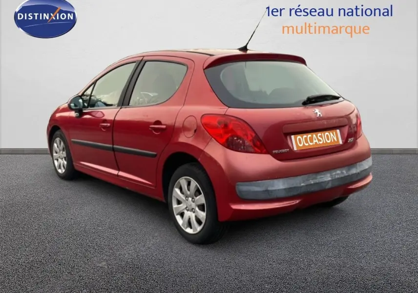 Vue 3/4 arrière droite d'une Peugeot 207 rouge métal cinq portes, avec plaques d'occasion visibles.