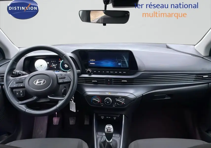 Vue intérieure avant du tableau de bord et volant de la Hyundai i20 2025 avec écran tactile et boîte manuelle.