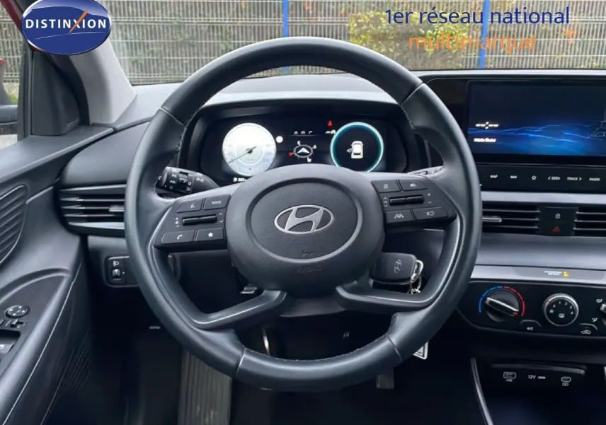 Vue intérieure centrée sur le volant noir de la Hyundai i20 2025, avec tableau de bord digital et écran tactile visible.
