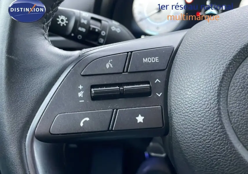 Gros plan sur les commandes gauche du volant en cuir noir de la Hyundai i20 2025, avec boutons multifonctions visibles.