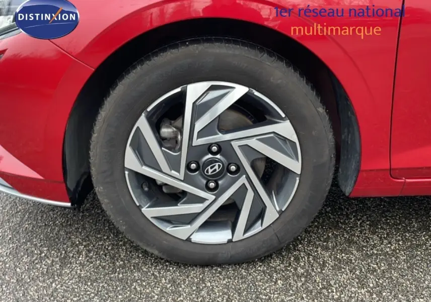 Gros plan sur la roue avant gauche d'une Hyundai i20 rouge Dragon Metal avec jante alliage au design géométrique.