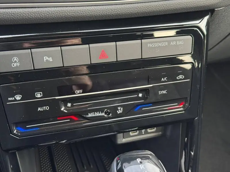 Détail de la console centrale noire du Volkswagen T-Cross blanc 2025, montrant les commandes de climatisation et les boutons de sécurité.