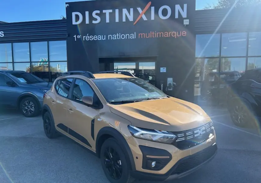 Vue 3/4 avant droite d'une Dacia Sandero Stepway beige Safari avec jantes noires et barres de toit grises.