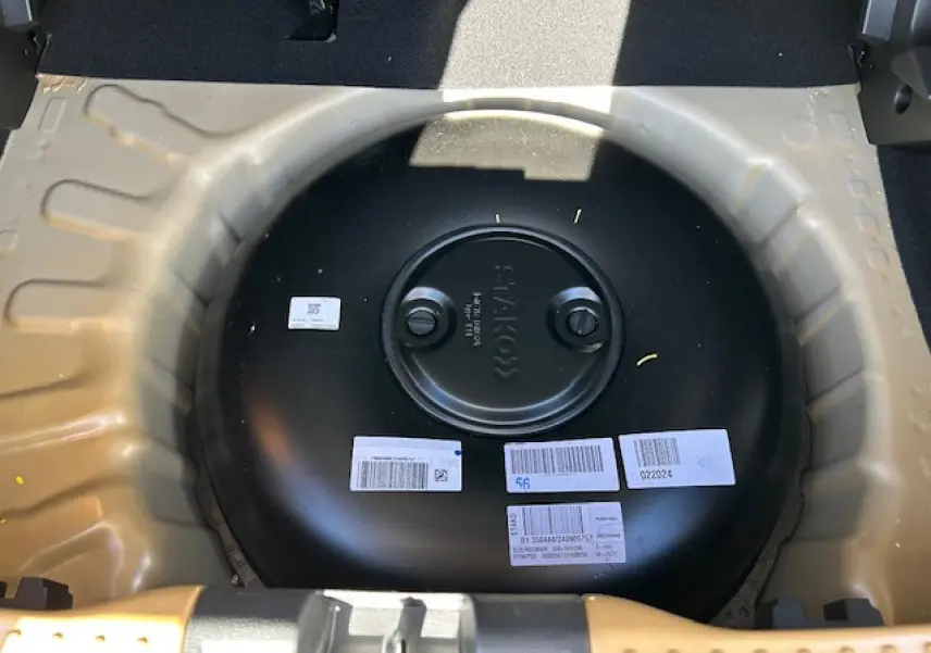 Vue plongeante sur le réservoir GPL noir dans le coffre beige Safari d'une Dacia Sandero III Stepway 2025.