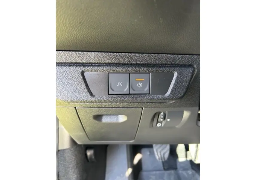 Gros plan sur les commandes LPG et verrouillage sous le tableau de bord d'une Dacia Sandero beige Safari.