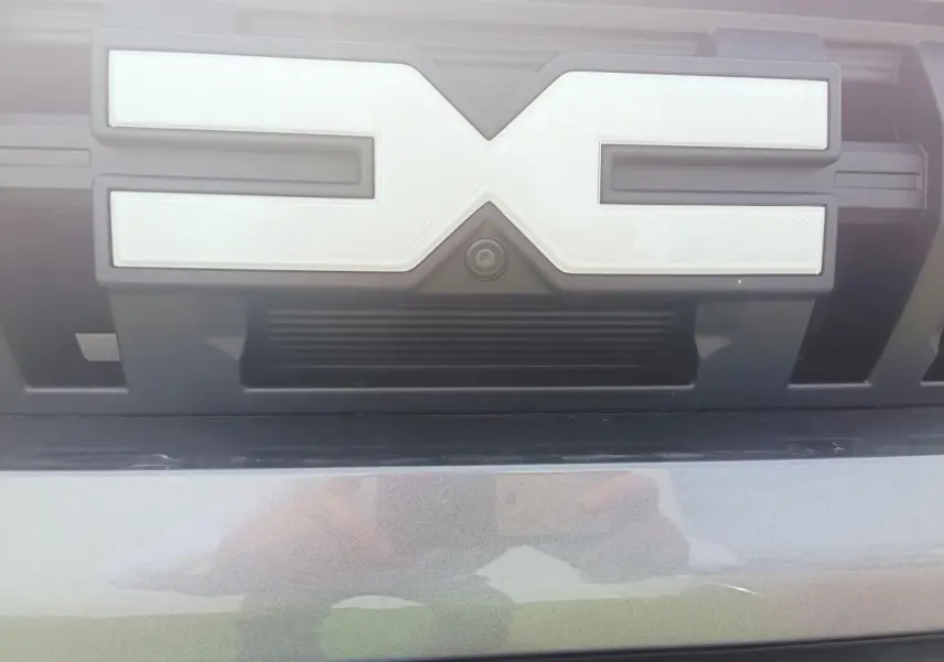 Gros plan sur la calandre avant gris schiste métallisé du Dacia Duster III avec caméra intégrée sous le logo.