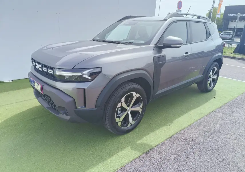 Dacia Duster III gris schiste métal en 3/4 avant droit, avec jantes alliage diamantées et barres de toit noires.