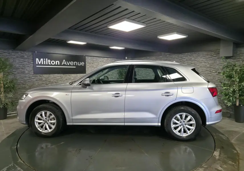 Audi Q5 gris en profil droit dans un showroom, avec jantes alliage et toit ouvrant visible.