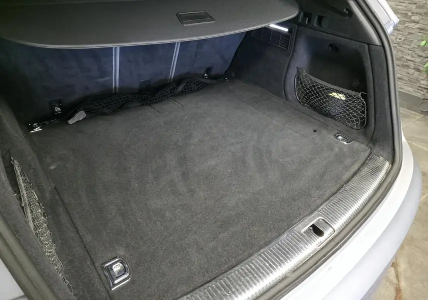 Coffre ouvert vu de l'arrière d'un Audi Q5 gris, avec tapis de sol noir et filet de rangement latéral.