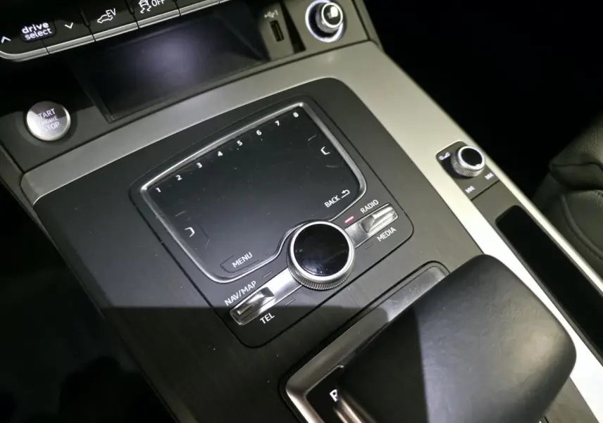 Gros plan sur la console centrale noire et grise de l'Audi Q5 S line avec commandes multimédia et bouton start/stop.