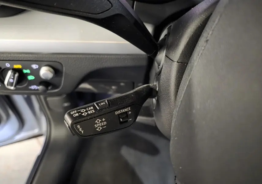 Gros plan sur la commande de régulateur de vitesse adaptatif côté gauche du volant dans l’habitacle gris d’un Audi Q5 hybride rechargeable.