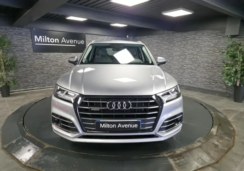 Vue frontale d'un Audi Q5 gris métallisé S line avec calandre noire et phares LED dans un showroom.
